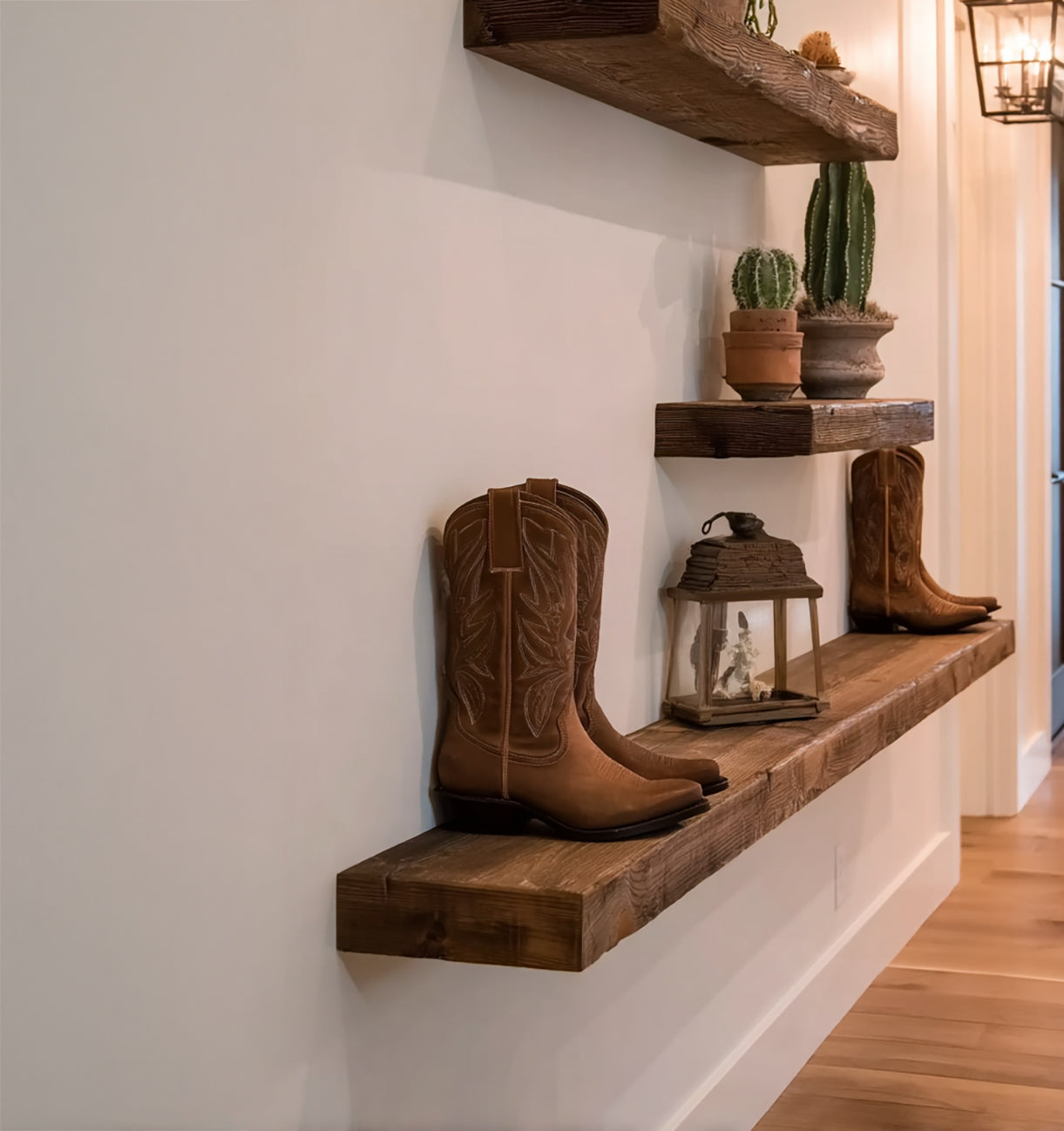 Rustic wooden floating shelves with brown cowboy boots, small lantern, and potted cacti in hallway