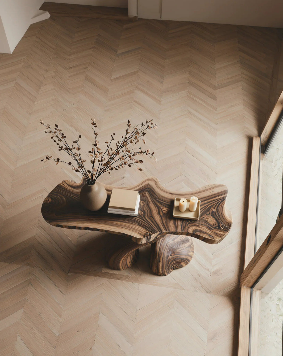 Live edge solid wood coffee table with natural grain, vase, books, and candles on herringbone floor