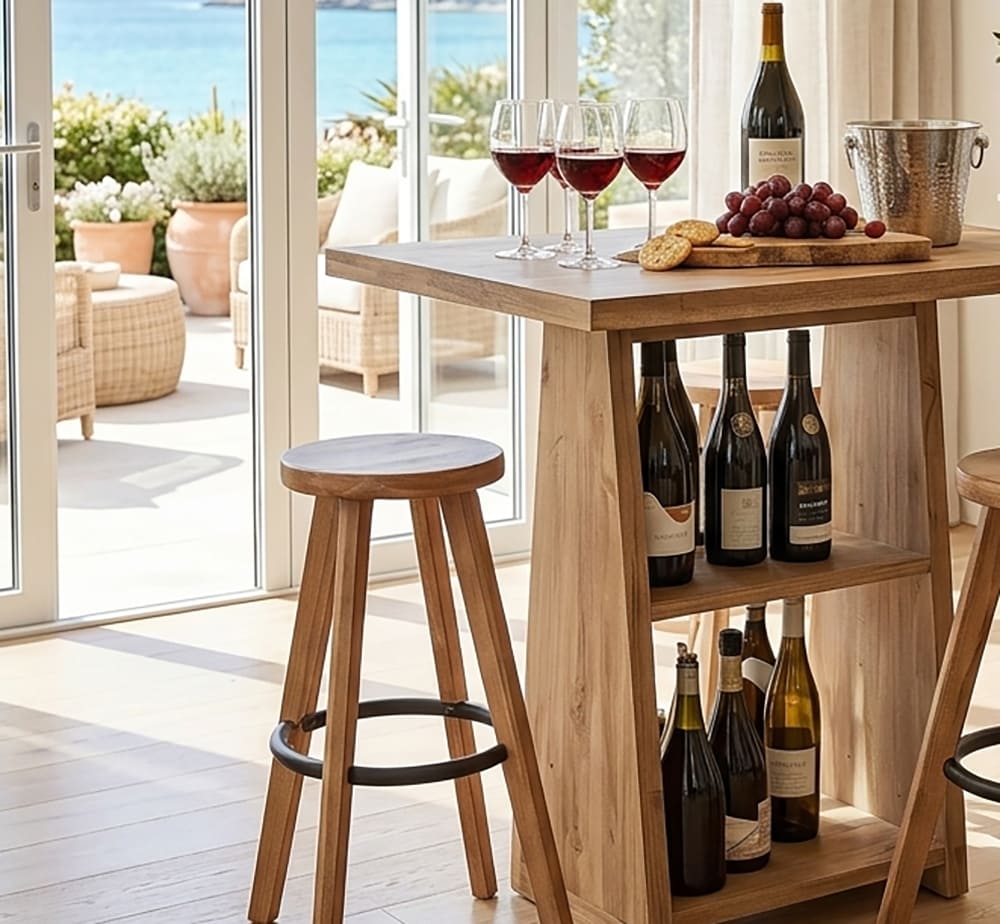 Natural wood balcony bar table set with wine glasses next to a sunny window with ocean view