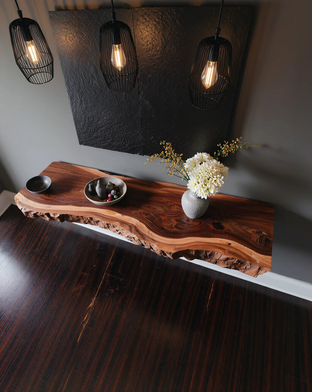 Live edge wood console table with ceramic vase, modern pendant lights, and decorative bowl