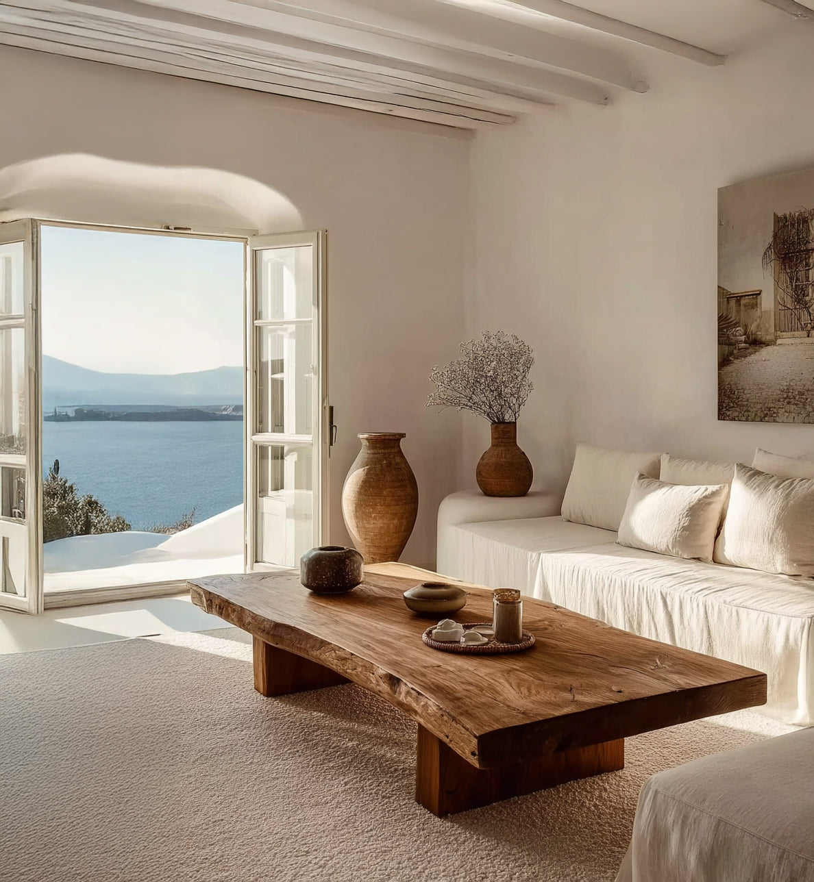 Bright living room with natural wood coffee table, white sofa, pottery, and sea view through open doors